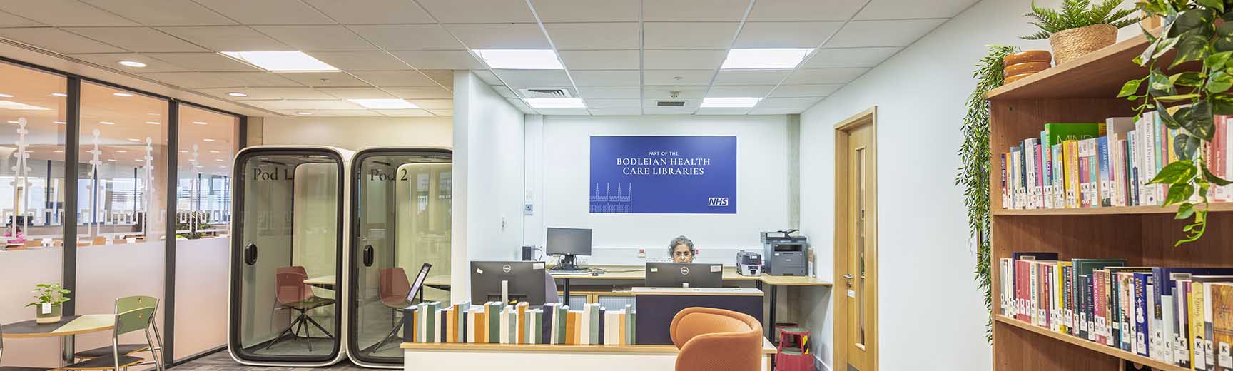 A library space with meeting pods on the left, a help desk in the centre and bookshelves on the right