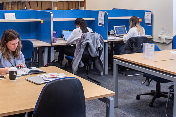 Tables in a room - some have blue separators - students are dotted about working at the desks